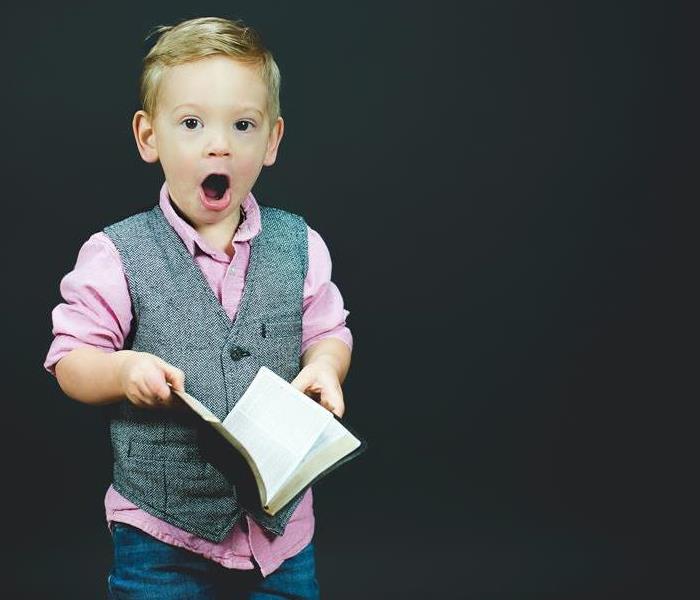 A small boy holding a book with his mouth open.